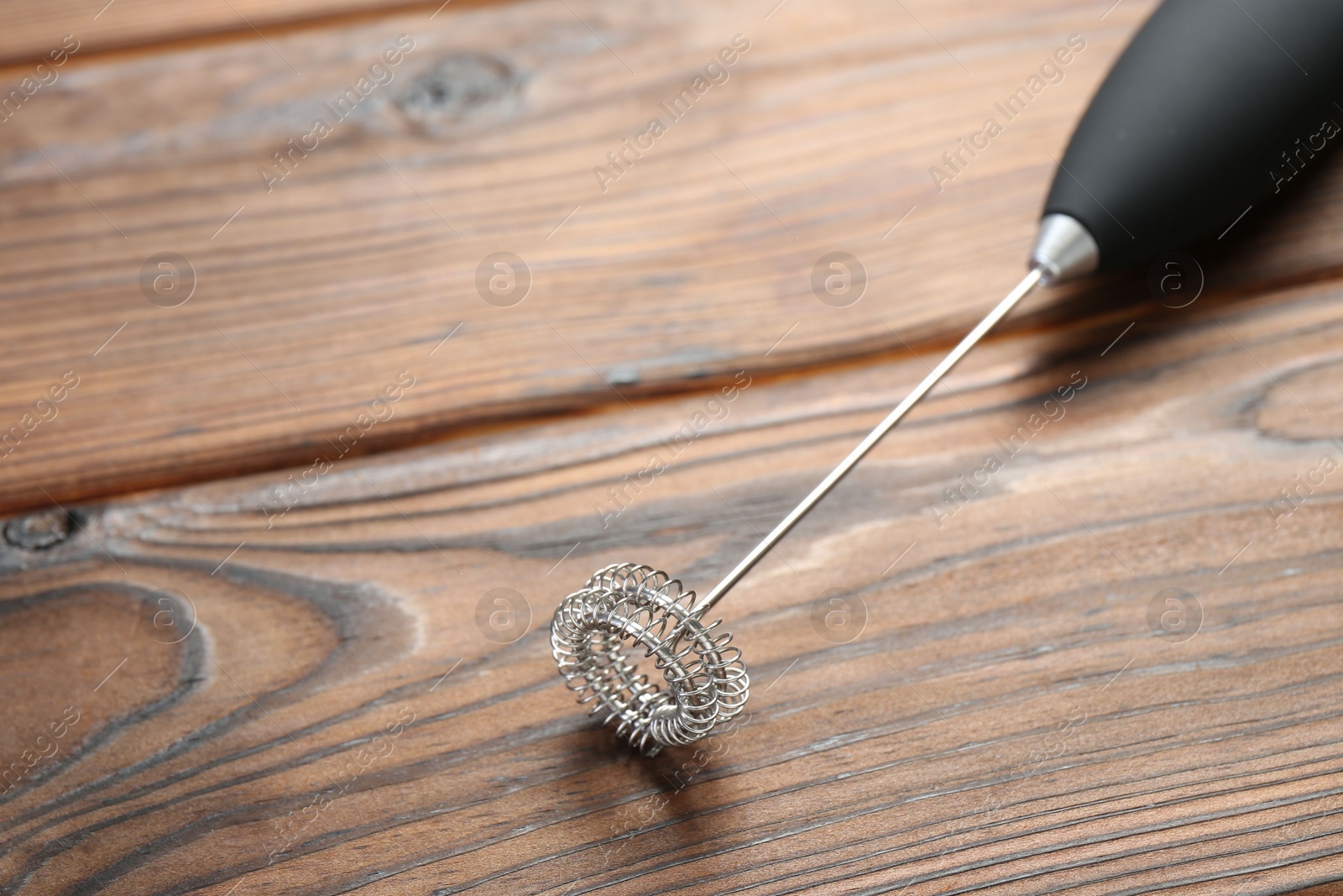 Photo of Black milk frother wand on wooden table, closeup. Space for text