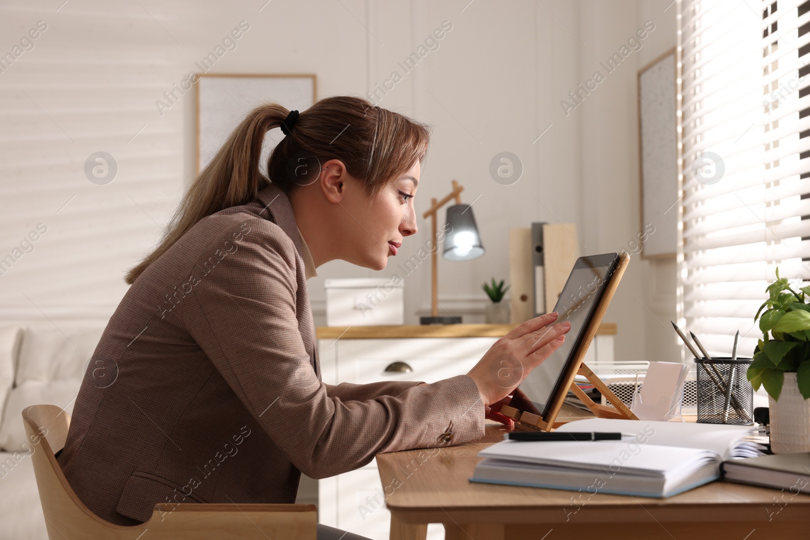 Photo of Young woman with poor posture using tablet at table indoors