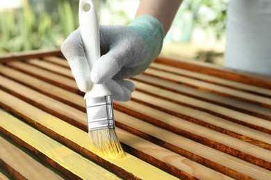 Photo of Woman painting wooden surface with yellow dye outdoors, closeup
