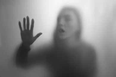 Photo of Silhouette of ghost behind fabric against light grey background. Black and white effect