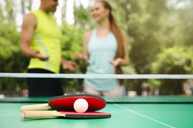 Photo of Couple talking near ping pong in park, focus on rackets and ball
