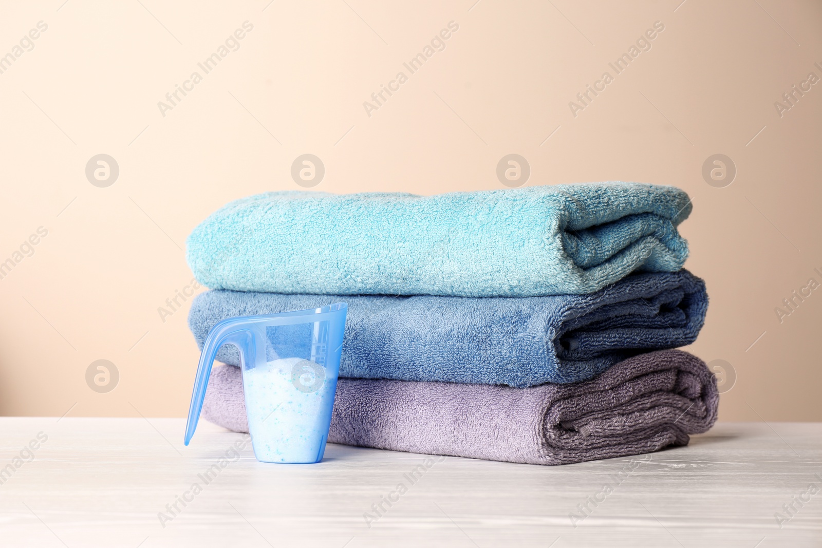 Photo of Measuring cup with washing powder and clean towels on table against color background. Laundry day