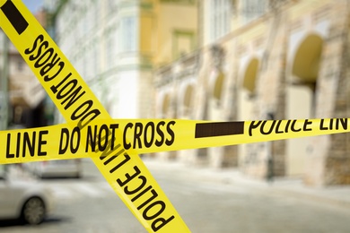 Image of Yellow police tape isolating crime scene. Blurred view of city street