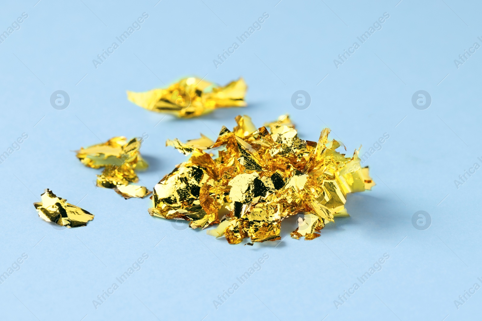Photo of Many pieces of edible gold leaf on light blue background, closeup