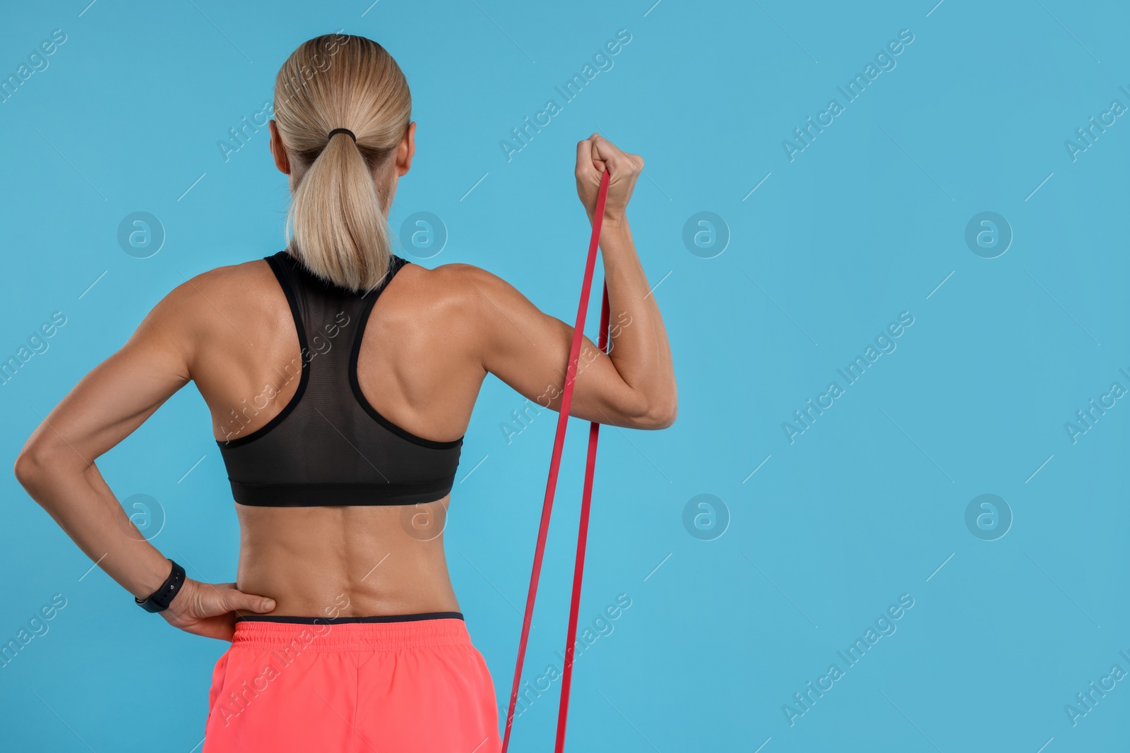 Photo of Woman exercising with elastic resistance band on light blue background, back view. Space for text