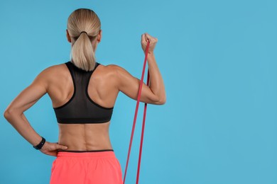 Photo of Woman exercising with elastic resistance band on light blue background, back view. Space for text