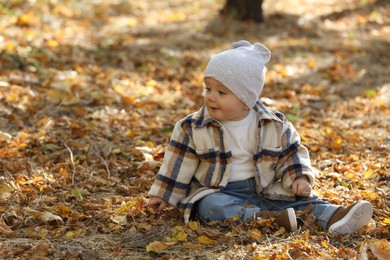 Photo of Cute little child on ground with dry autumn leaves outdoors, space for text