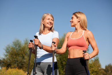 Happy women practicing Nordic walking with poles outdoors on sunny day