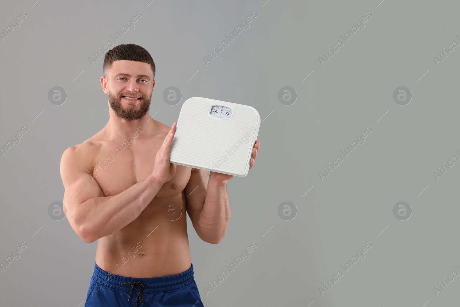 Photo of Happy athletic man holding scales on grey background, space for text. Weight loss concept