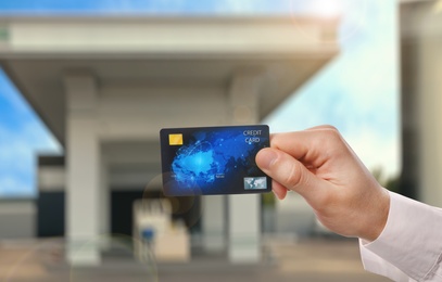 Image of Man holding credit card against blurred gas station, closeup. Cashless payment