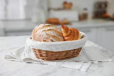 Photo of Wicker bread basket with freshly baked loaf and croissant on white marble table in kitchen