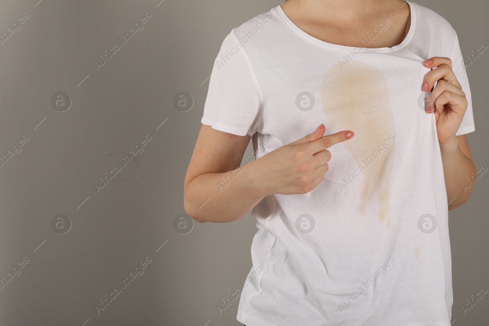 Photo of Woman showing stain from coffee on her shirt against light grey background, closeup. Space for text