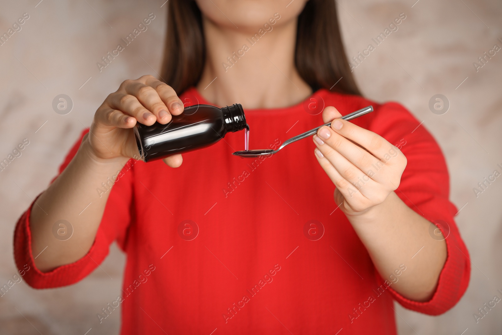 Photo of Woman pouring cough syrup into spoon on blurred background, closeup