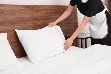 Chambermaid making bed in hotel room, closeup