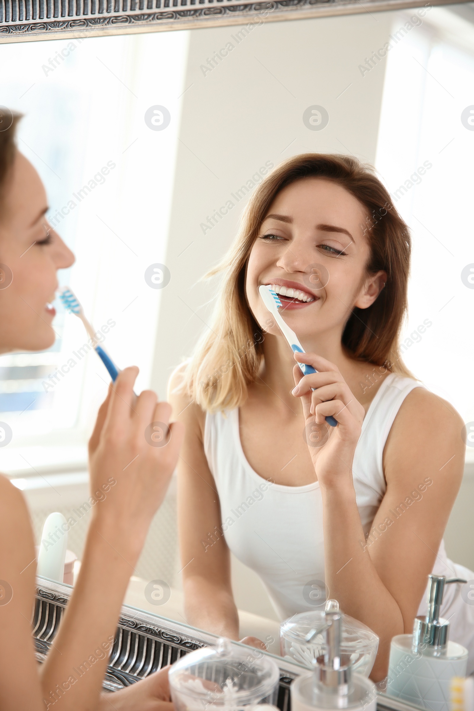 Photo of Young beautiful woman with toothbrush near mirror in bathroom. Personal hygiene