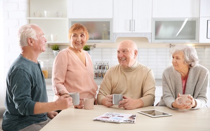 Elderly people spending time together at table in kitchen