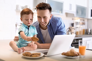 Photo of Young father and his cute little son with cookies in kitchen