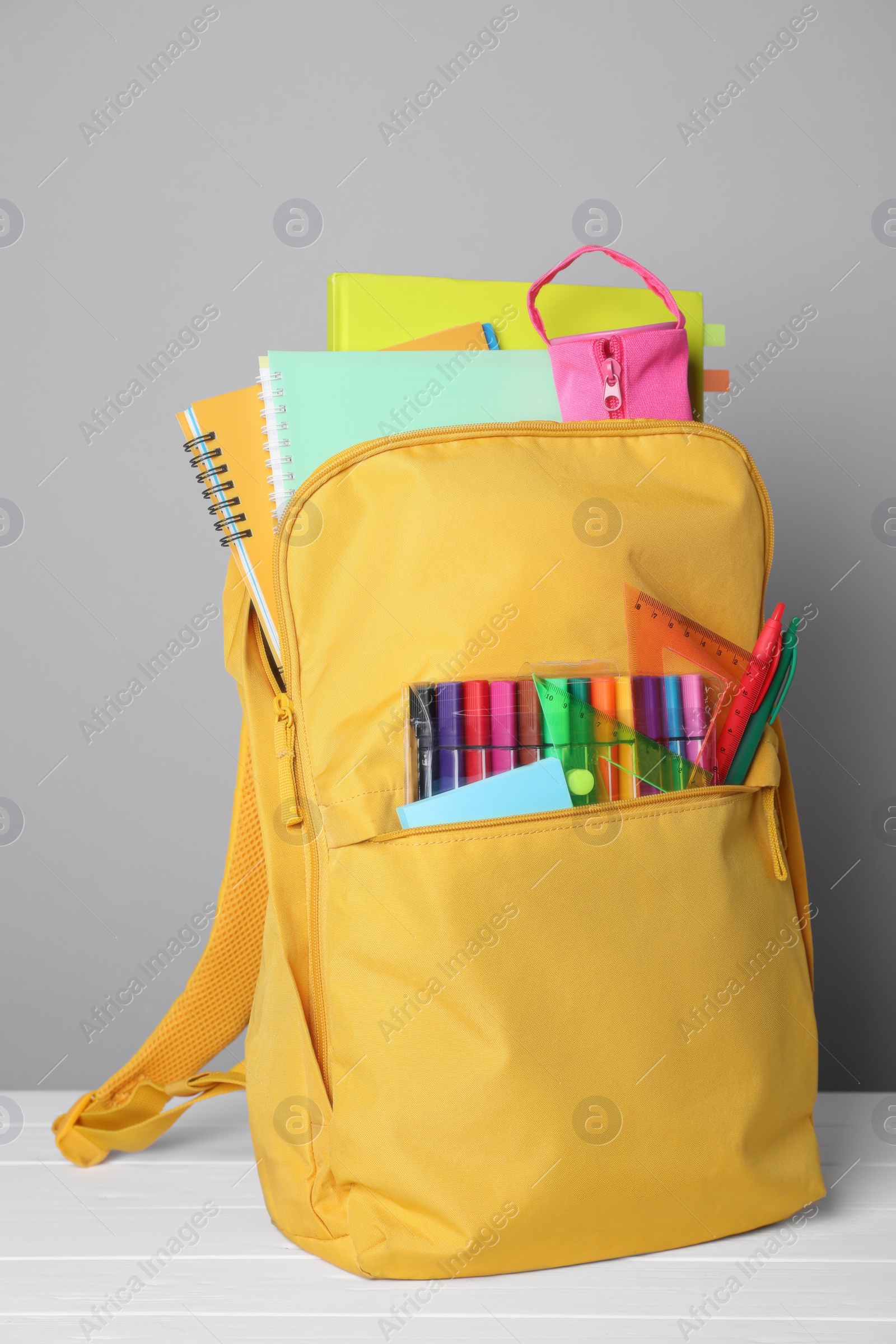 Photo of Yellow backpack with different school stationery on white table against grey background