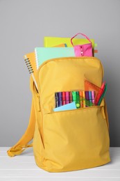 Yellow backpack with different school stationery on white table against grey background
