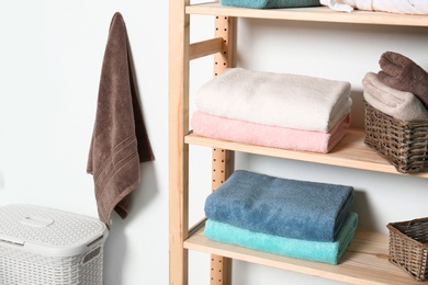 Shelving unit with clean towels near white wall in modern bathroom interior