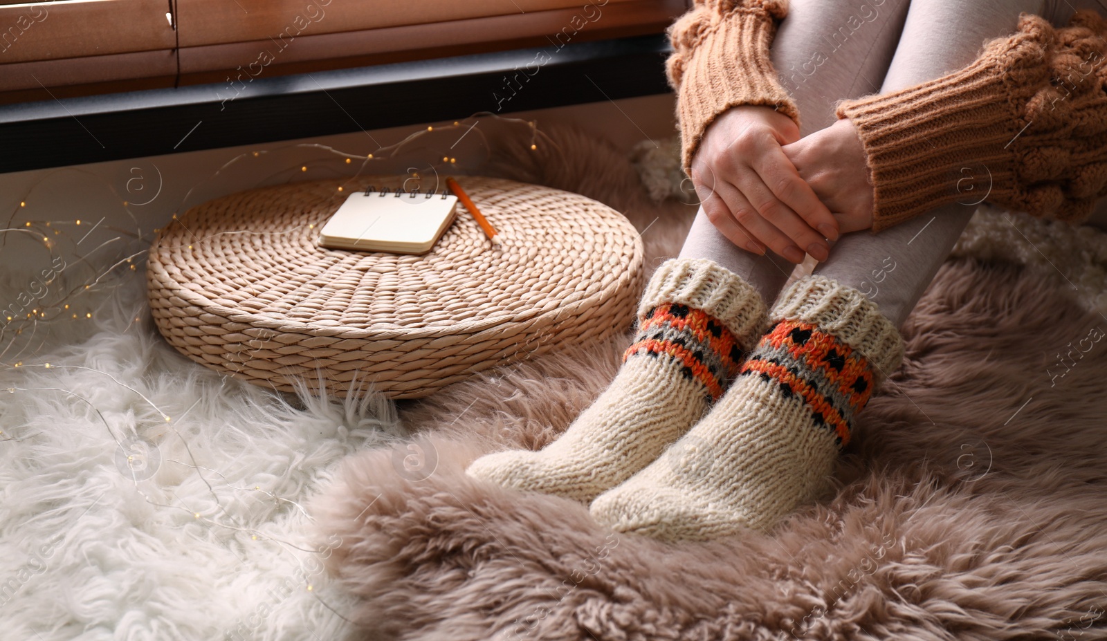 Photo of Woman wearing knitted socks on window sill indoors, closeup. Warm clothes