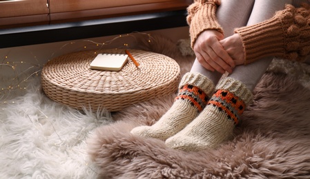 Woman wearing knitted socks on window sill indoors, closeup. Warm clothes