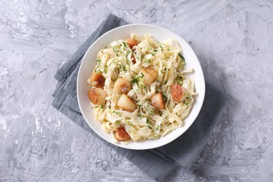 Photo of Delicious scallop pasta with spices in bowl on gray textured table, top view