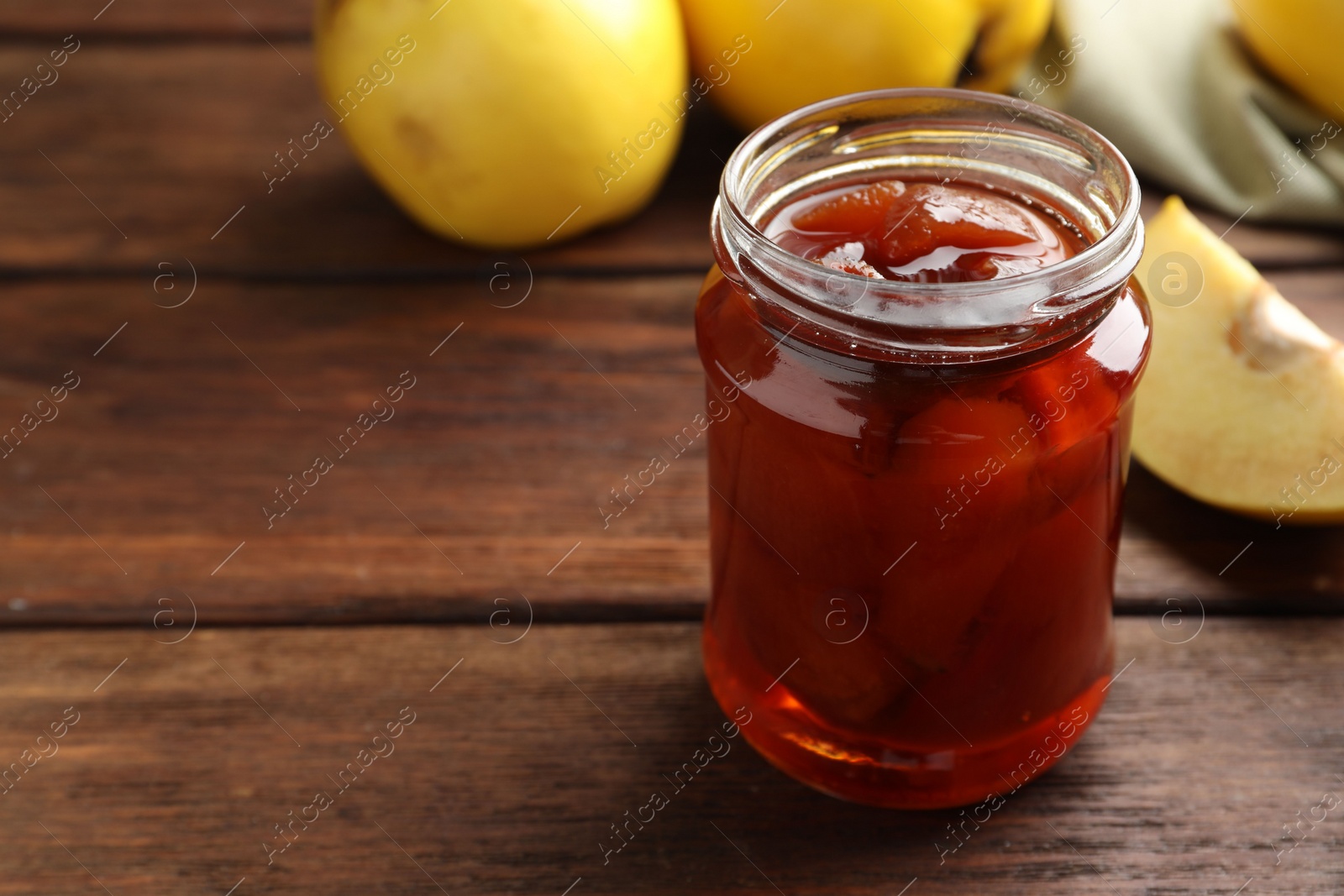 Photo of Tasty homemade quince jam in jar on wooden table, closeup. Space for text