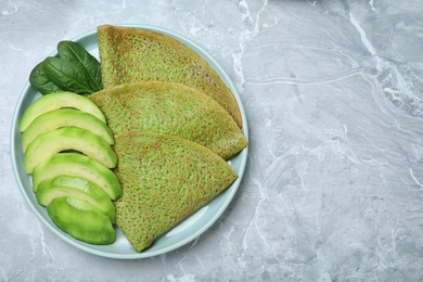 Delicious spinach crepes with avocado on marble table, top view. Space for text