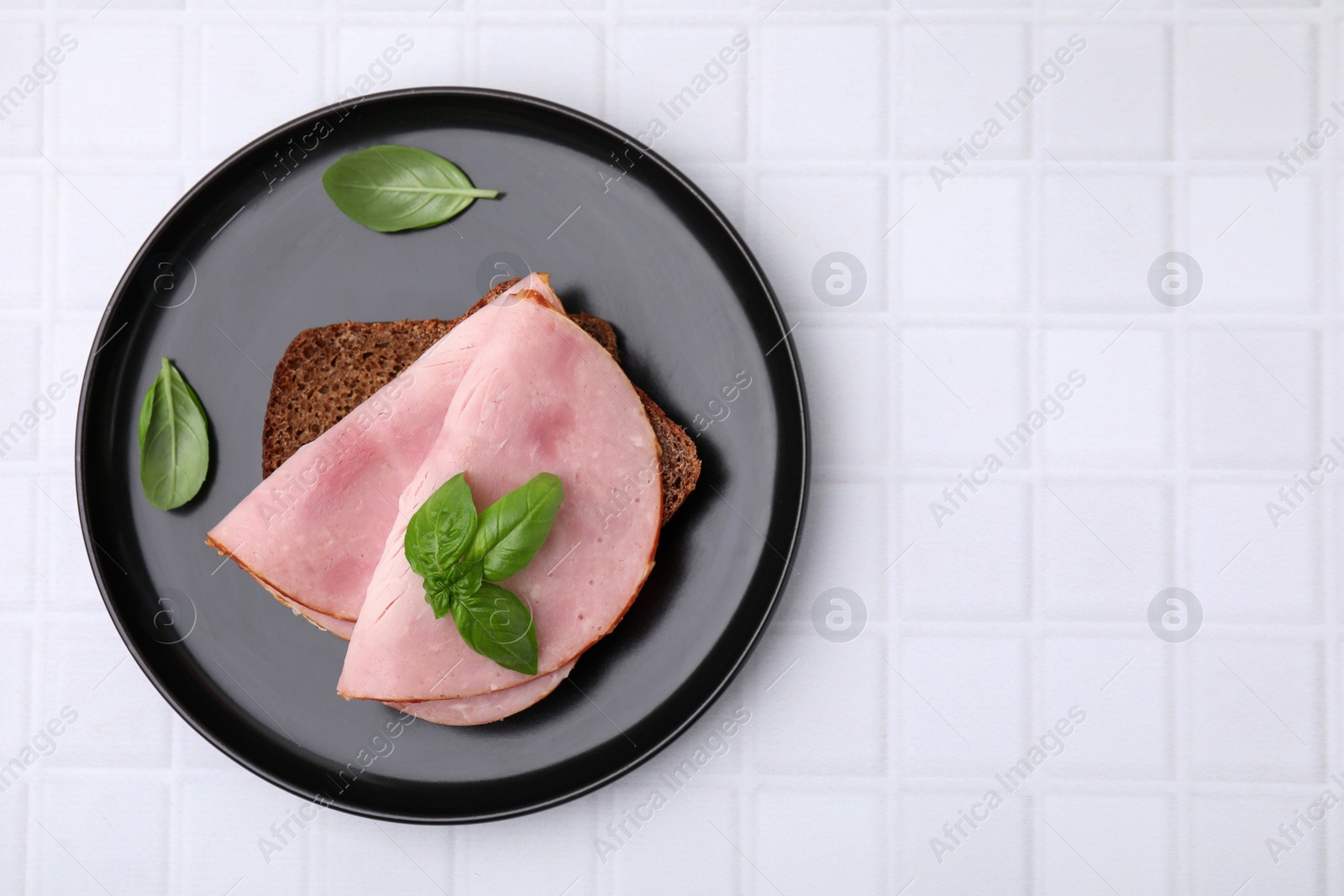 Photo of Delicious sandwich with ham on white tiled table, top view. Space for text