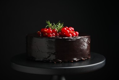 Photo of Tasty homemade chocolate cake with berries and rosemary on dessert stand against black background