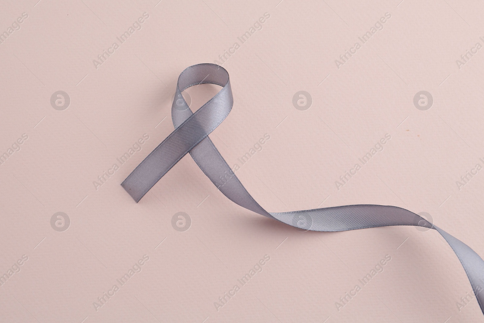 Photo of Grey awareness ribbon on beige background, top view