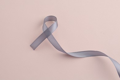 Photo of Grey awareness ribbon on beige background, top view