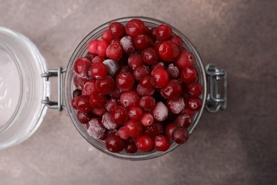 Photo of Frozen red cranberries in glass jar on brown textured table, top view