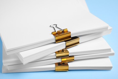 Photo of Many sheets of paper with golden clips on light blue background, closeup