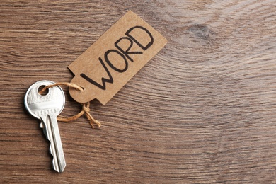 Metal key with tag on wooden table, top view and space for text. Keyword concept