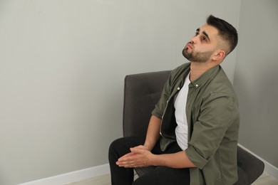 Sad man sitting near light grey wall. Space for text