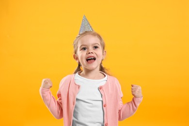 Photo of Birthday celebration. Cute little girl in party hat on orange background