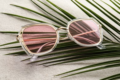 Stylish sunglasses and palm leaf on sand, above view