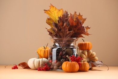 Photo of Composition with beautiful autumn leaves, berries and pumpkins on table against beige background