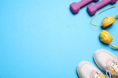 Dumbbells, headphones and sneakers on light blue background, flat lay. Space for text