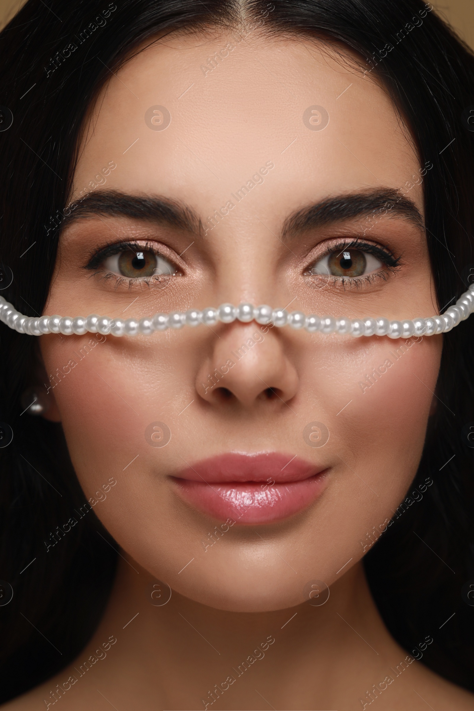 Photo of Young woman with elegant pearl jewelry on brown background, closeup