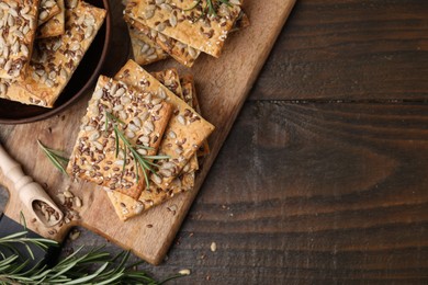 Photo of Cereal crackers with flax, sunflower, sesame seeds and rosemary on wooden table, top view. Space for text