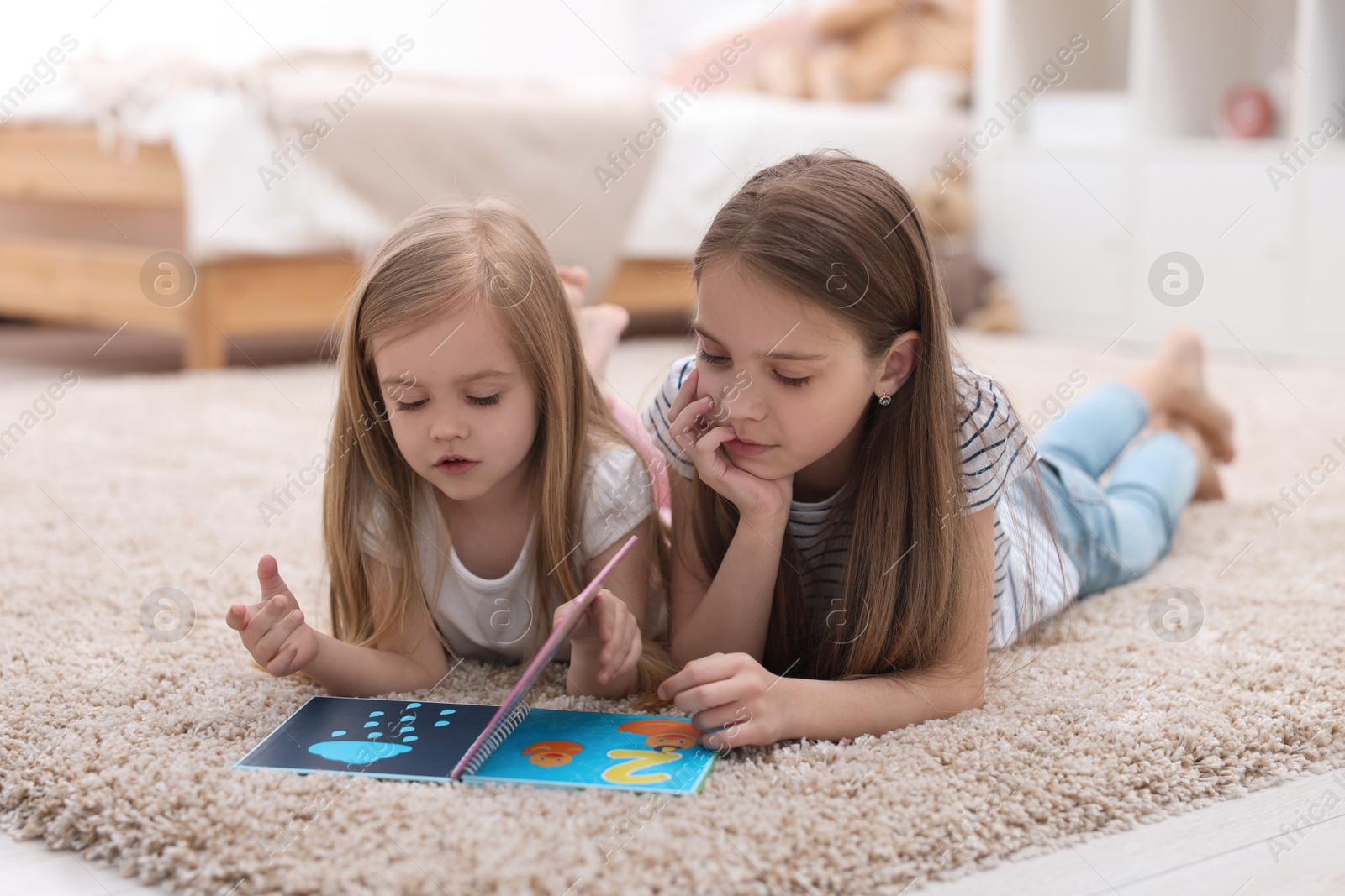 Photo of Cute little sisters reading book together at home