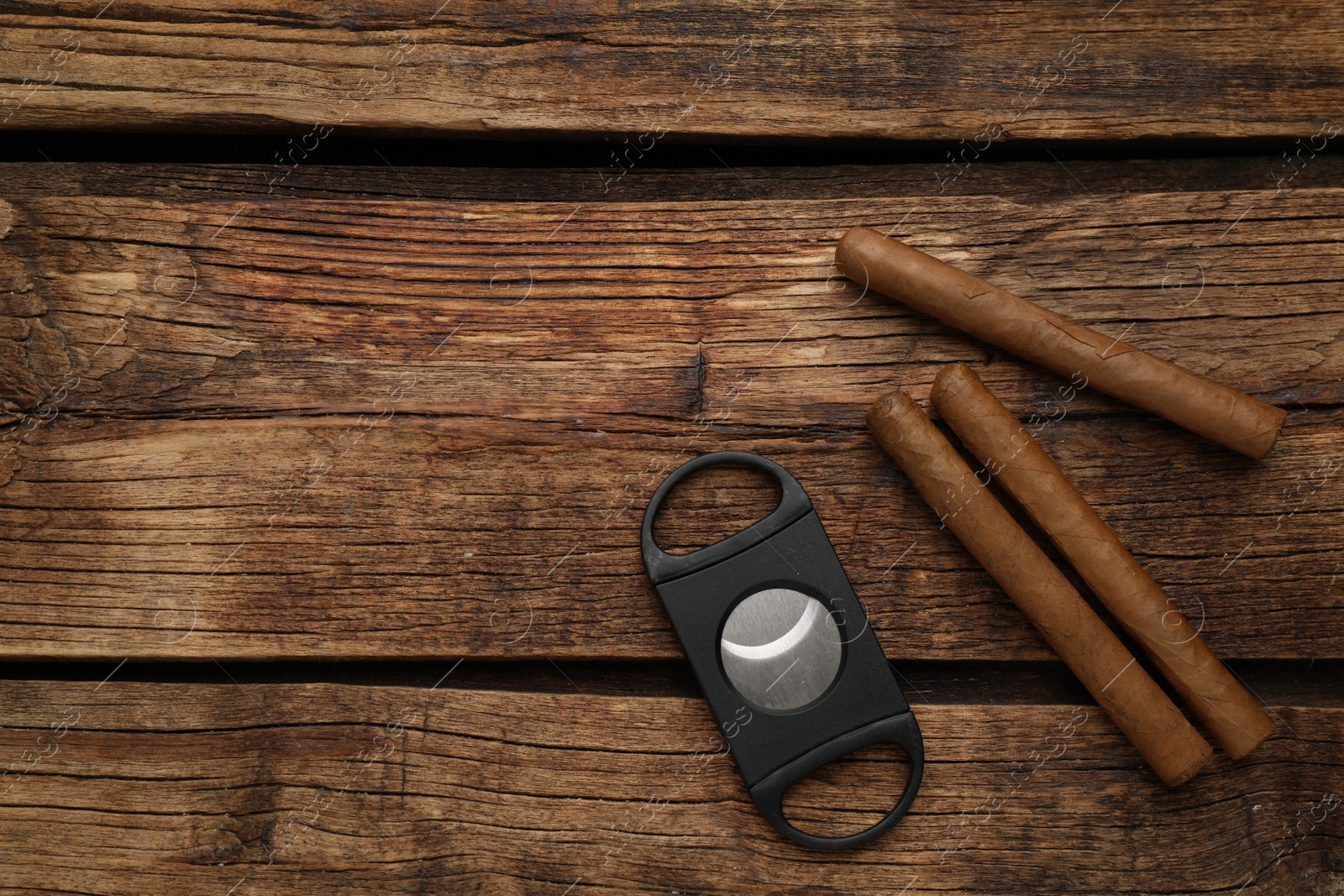 Photo of Cigars and guillotine cutter on wooden table, flat lay. Space for text