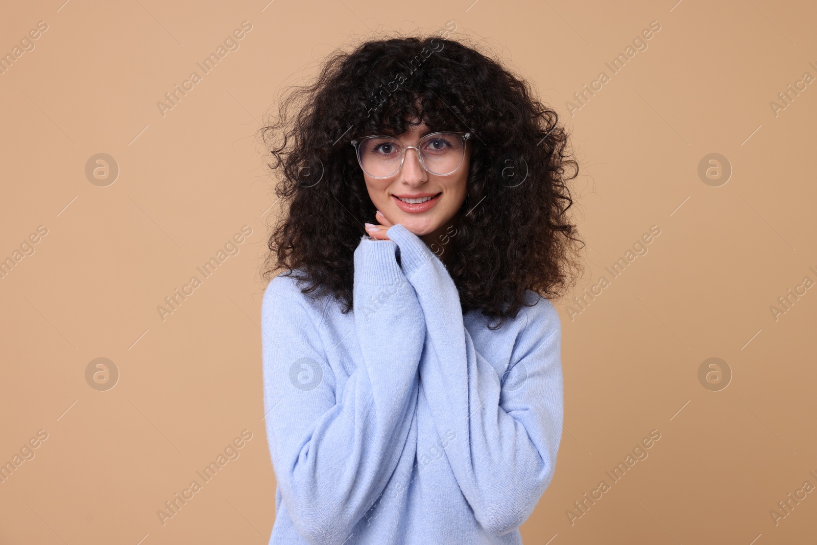 Photo of Happy young woman in stylish light blue sweater and glasses on beige background