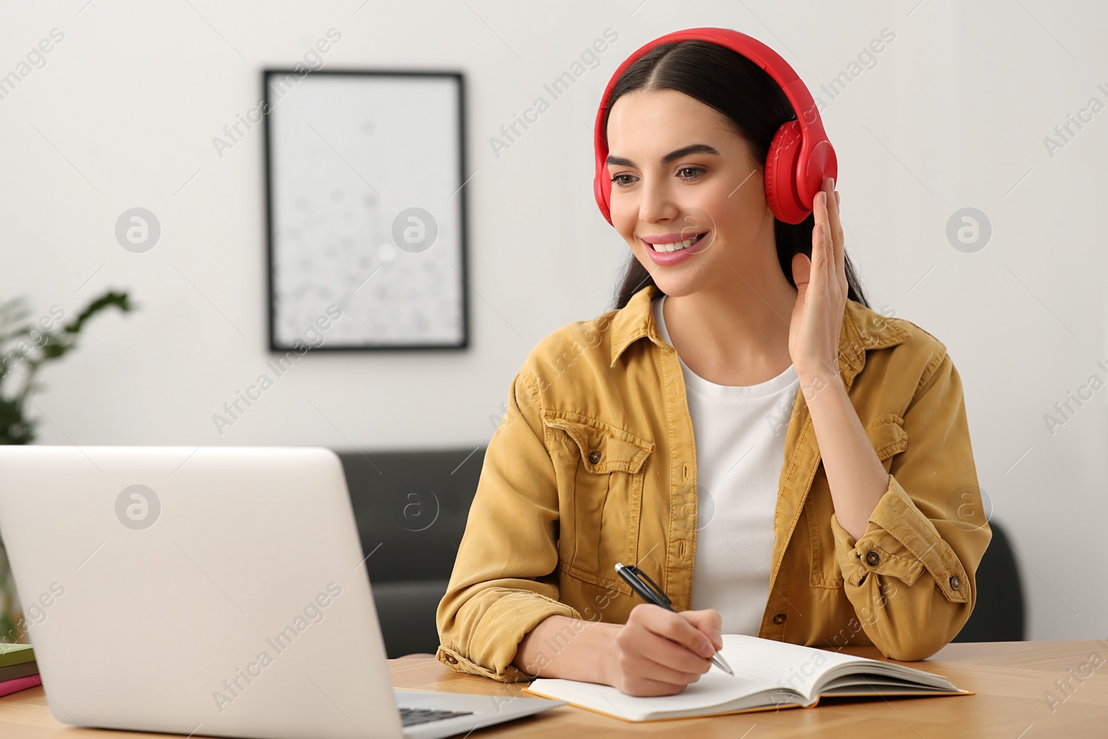 Photo of Online translation course. Student in headphones writing near laptop at home