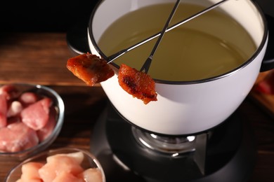 Fondue pot, forks with fried meat pieces and other products on wooden table, closeup. Space for text
