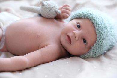 Photo of Cute newborn baby in warm hat with toy on bed