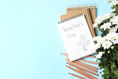 Photo of Notebook with phrase Teacher's Day and beautiful white flowers on light blue background, flat lay. Space for text